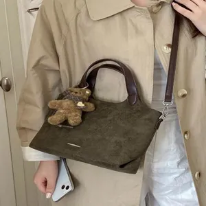 Brown faux suede tote bag with leather handles and shoulder strap, carried with a plush charm
