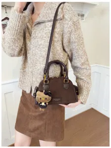 Sac brun à texture daim porté en bandoulière, avec poignées foncées et pendentif chat en peluche