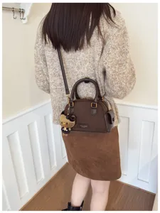 Vue de dos d’un modèle portant un sac brun effet daim, avec bandoulière et breloque chat en peluche