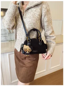 Détail du sac noir en suédine porté en bandoulière, avec ferrures dorées et breloque en peluche