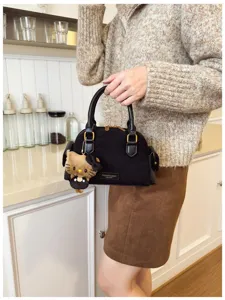 Une personne tient un sac noir effet daim, à anses, avec ferrures dorées et pendentif ourson