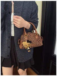 Vue rapprochée d’un sac léopard porté à la main, avec anses brunes et breloque chat en peluche