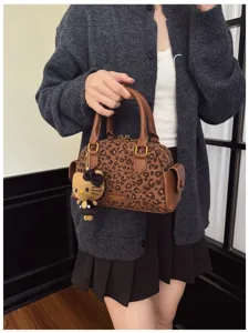 Une personne porte un sac à imprimé léopard, avec des poignées brunes et un pendentif décoratif en peluche