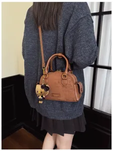 Vue de dos d’un modèle portant un petit sac brun texturé, avec anses, bandoulière et pendentif doux