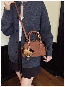 Sac brun à texture suédée porté en bandoulière, avec un pendentif chat en peluche sur le côté