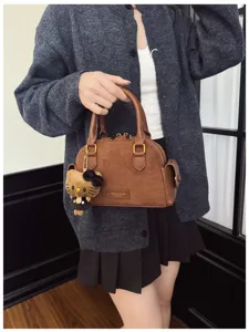 Sac brun porté, à texture daim, avec ferrures dorées et un charm d’ours en peluche