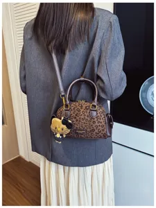 Sac rond à imprimé léopard porté en bandoulière sur un blazer gris, avec un pendentif chat