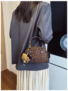 Sac à imprimé léopard porté sur un blazer gris, avec pendentif peluche et détails dorés.