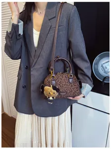 Le modèle porte un mini-sac léopard aux poignées brunes, ferrures dorées et charm en peluche