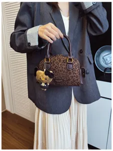 Sac à imprimé léopard, poignées brun foncé et breloque chat en peluche, présenté tenu à la main.