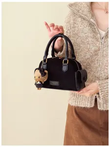 Détail d’un sac noir en velours, avec poignées en cuir, pièces dorées et breloque en peluche