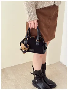 Modèle tenant un sac noir à texture suédée, bordure façon cuir et petit ourson en peluche