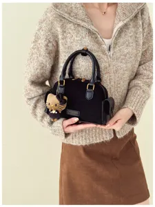 Une femme présente un petit sac en suédine noire, avec des détails dorés et un charm chat en peluche
