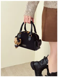 Une femme tient un sac noir effet daim, avec ferrures dorées et pendentif ours en peluche