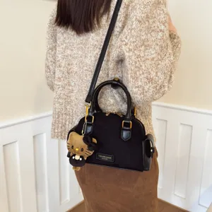Sac Boston noir en suédine, poignées en cuir, détails dorés et breloque ours, porté en bandoulière