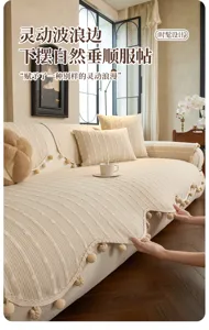 Living room view of a cream textured sofa cover with a wavy pom-pom fringe draped over the seat
