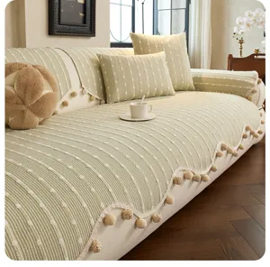 Close view of a pale green textured sofa cover with white dotted stripes and beige pom-pom trim