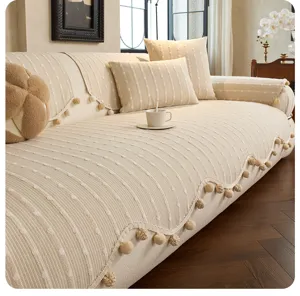 Living room view of a cream sofa cover with raised ribbed texture and tan pom-pom fringe