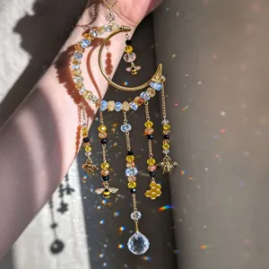 Close-up of a gold crescent suncatcher with crystal beads, bee and honeycomb charms in sunlight