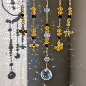 Gold chains with faceted amber beads, bee and honeycomb charms, and a crystal catching sunlight