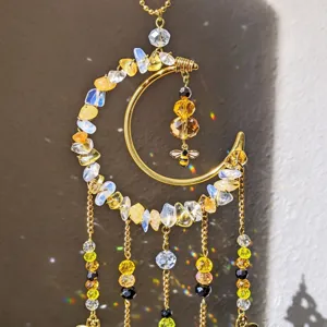 Close-up of a gold crescent with crystal chips, a bee charm and dangling chains catching sunlight