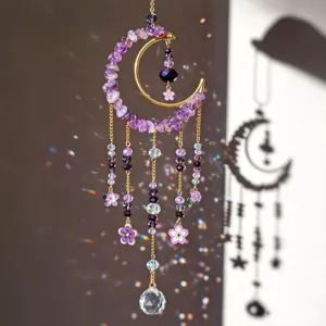 Close-up of a crescent suncatcher with purple stones, flower charms and crystal drops in sunlight