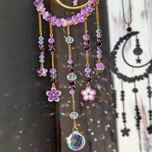 Close-up of purple crystal beads, gold chains, flower charms and a faceted pendant casting rainbow light