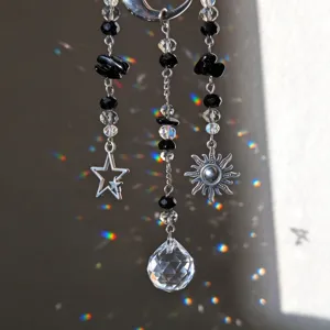 Detalle de cuentas negras y cristales claros, con dijes de estrella y sol y un cristal colgante