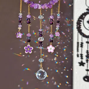 Close-up of purple crystal strands, gold chains, flower charms and a faceted sphere in rainbow light