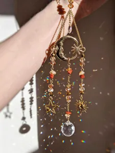 Primer plano de un colgante dorado de luna y sol, con cuentas facetadas y una gota de cristal