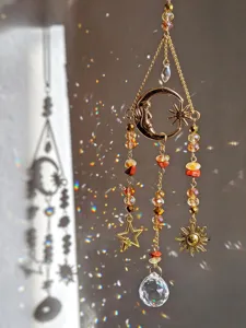 Detalle de un adorno dorado de luna y sol, con cuentas rojas y ámbar y un colgante de cristal