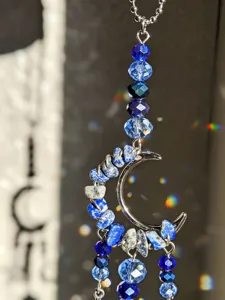 Primo piano di perline blu e frammenti di pietra attorno a una mezzaluna argentata con fili pendenti