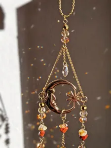 Detalle de un colgante dorado de luna y estrella, con cuentas facetadas y piedras rojas y amarillas