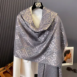 Grau-taupefarbener Jacquardschal über einem weißen Mantel, mit Muster und Fransenkanten