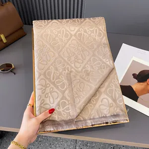 Beigefarbener Jacquard-Schal mit Rautenmuster aus Buchstaben und Fransen, gefaltet präsentiert