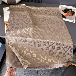 Dettaglio in piano di un tessuto tortora con cuori e macchie leopardate intrecciati, con frange