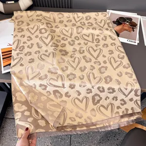 Vista ravvicinata di una sciarpa beige con cuori e motivi leopardati, rifinita con frange