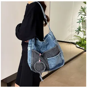 A model carries a two-tone washed denim shoulder bag with patch pockets and a round coin pouch