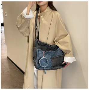 Woman wearing a dark gray and light blue denim shoulder bag with a round charm and tassel