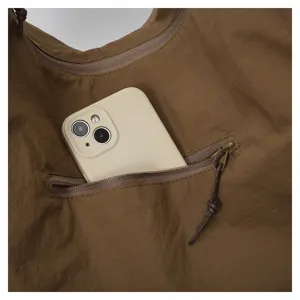 Nahaufnahme der Reißverschluss-Innentasche einer braunen Nylontasche mit Handy und Lederanhänger