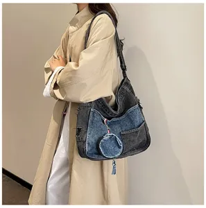 Two-tone denim shoulder bag worn crossbody, with a detachable coin pouch and a hanging tassel