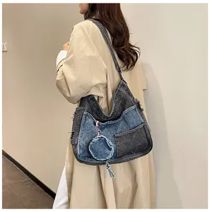 Shoulder-worn denim bag with gray and blue patchwork, front pocket, round coin pouch and tassel