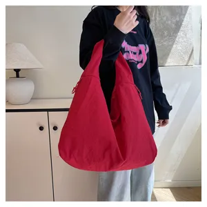 Rote, geräumige Nylontasche mit Schulterriemen und geknitterter Oberfläche, getragen im Wohnbereich