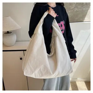Detailansicht einer getragenen elfenbeinfarbenen Tasche mit breiten Henkeln und weichem Faltenwurf