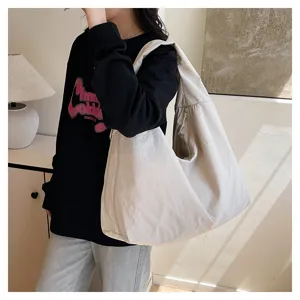 Eine Person trägt drinnen eine große cremeweiße Schultertasche aus weichem Stoff mit lockerer Form.