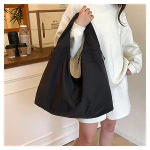 Person trägt eine große schwarze Schultertasche in Nylonoptik mit seitlichen Kordelzügen
