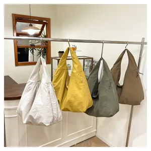 Vier geknitterte Stofftaschen in Elfenbein, Senfgelb, Oliv und Khaki hängen an einer Metallstange.