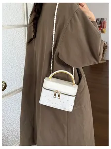 Borsa bianca con stelle, manico dorato e tracolla a catena sopra un cappotto marrone