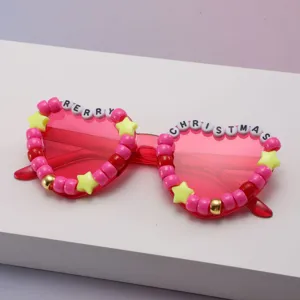 Pink transparent sunglasses with bead, star and festive letter decorations on a pale surface