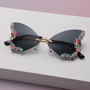Lunettes papillon, verres dégradés foncés, pont doré et perles colorées sur les bords.